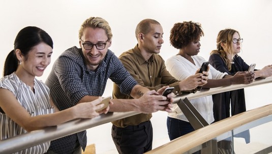 5 people using the Limitless app on their phones whilst leaning on a fence.